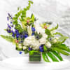 Mixed bouquet in a square glass vase with white, green, and blue flowers