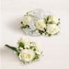 Two white rose boutonnieres with ribbon accents on a light background