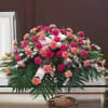 Pink and peach floral casket spray with white ribbon accents