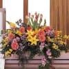 Large mixed floral arrangement with yellow lilies and pink blooms on a casket