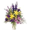 Mixed bouquet with yellow lilies, purple flowers, and pink roses in a clear vase