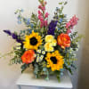 Colorful mixed bouquet with sunflowers, roses, and tall blue and pink blooms in a vase