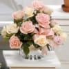 Pink and white roses arranged in a clear glass vase with a pink ribbon