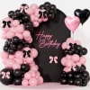 Pink and black balloon arch around a Happy Birthday backdrop