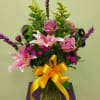 Pink roses and lilies in a glass vase with a yellow ribbon