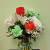 Bouquet of red roses, white daisies, and green carnations in a glass vase