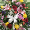 Standing floral spray with roses, lilies, and a white ribbon bow