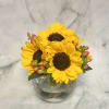 Yellow sunflowers in a round glass vase with pink berry accents