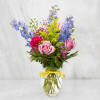 Mixed bouquet of pink roses, blue delphinium, and yellow filler in a glass vase