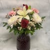 Mixed bouquet with red roses, white lilies, and pink carnations in a dark vase