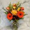 Bouquet of orange gerbera daisies and yellow-orange roses in a glass vase