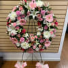 Pink and white floral wreath on a black stand with pink bows