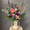 Tall mixed flower arrangement in a white handled vase with pink and purple blooms