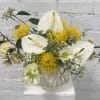 White anthuriums and yellow pincushion blooms in a white vase