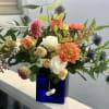 Asymmetrical bouquet of orange dahlias and cream roses in a cobalt blue glass cube vase