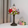 Stained-glass table lamp beside two artificial roses