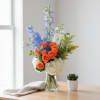 Bouquet of orange roses, blue delphinium, and white hydrangeas in a glass vase
