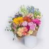 Large mixed-color bouquet with sunflowers, roses, peonies, and protea wrapped in kraft paper in a white cylinder.