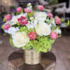Pink and white roses arranged in a gold vase with green hydrangea accents