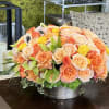 Low floral arrangement of peach, pink, and yellow roses in a silver bowl
