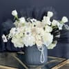 White floral arrangement in a ribbed blue vase with dark feather accents