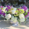 White roses and hydrangeas with purple orchids in a pedestal vase
