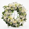 White floral wreath with roses, lilies, and green accents on a stand