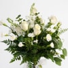 White roses and small white flowers in a clear vase with greenery