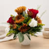Bouquet of red roses, white carnations, and bronze chrysanthemums in a white vase.