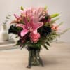 Pink lilies and roses arranged in a glass vase with black ribbon
