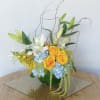 Arrangement of yellow roses, white lilies, and blue hydrangeas in a green vase