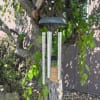 A silver wind chime hanging from a tree branch outdoors.