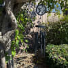 Black memorial wind chime with hummingbird design hanging from a tree over a rock garden.