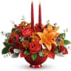 Red and orange floral arrangement in a red vase with two tall candles