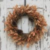 Autumn wreath with orange leaves, berries, and pinecones on a weathered white door