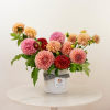 Pink and peach dahlias arranged in a white vase with a striped ribbon