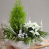 Holiday centerpiece with white poinsettias, evergreens, and silver ornaments in a white bowl
