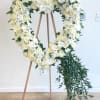 Heart-shaped white floral wreath on a wooden easel with trailing greenery