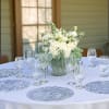 White floral centerpiece in a glass vase on a round table with wine glasses