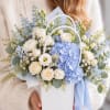 Blue and white flower arrangement in a white handled basket with ribbon