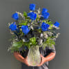 Blue roses arranged in a clear glass vase with mixed greenery