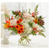 Mixed bouquet of roses, hydrangeas, and orange blooms in a clear glass vase