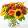 Bouquet of sunflowers, roses, and mums in a clear glass vase