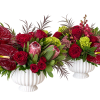 Two red floral arrangements in white urns with large anthuriums and roses