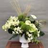 White and green floral arrangement in a white pedestal vase