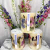 Three floral candles with pressed flowers and tall flower stems behind them
