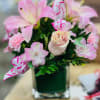 Pink lilies and roses arranged in a square glass vase
