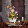Colorful ranunculus arrangement in a white footed bowl beside lit candles