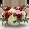 Red roses and pink blooms arranged with apples in a white bowl vase