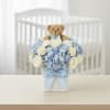 Teddy bear above a blue and white flower arrangement in a square box